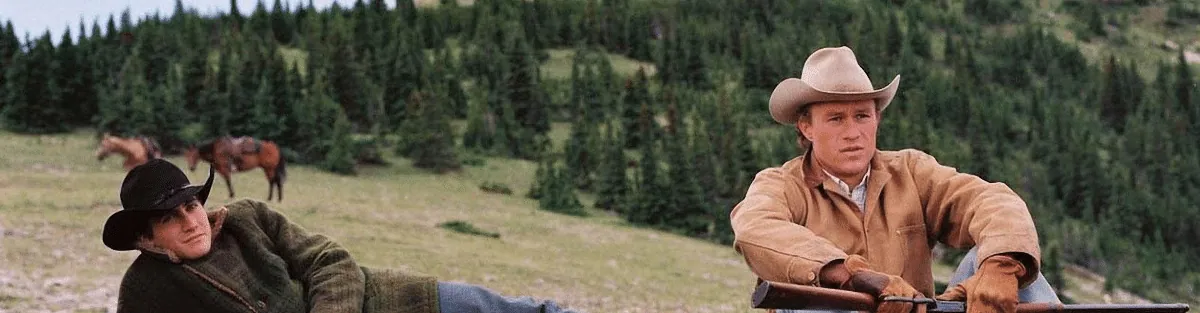 Film still from Brokeback Mountain: two cowboys rest in a mountain pasture, one reclining on the grass, the other seated near a truck.