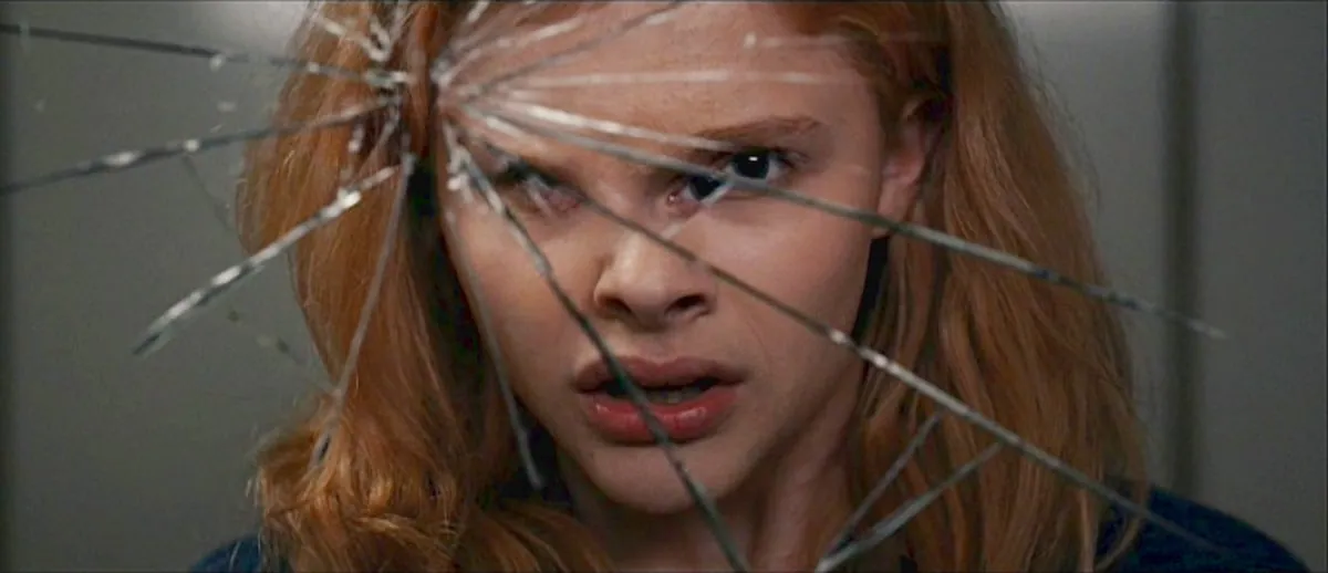 Film still from Carrie: Carrie's face seen through a web of shattered glass, her expression tense and wide-eyed.