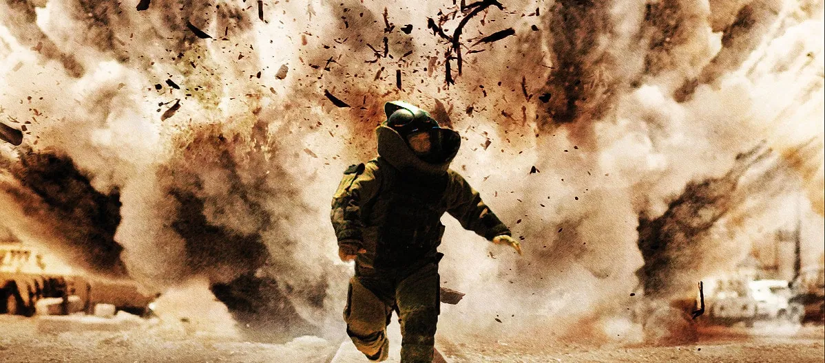Film still from The Hurt Locker: a bomb disposal technician in a blast suit runs as an explosion erupts behind him.
