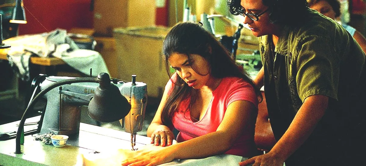 Film still from Real Women Have Curves: a woman concentrates at a sewing machine in a garment factory as a coworker looks on.