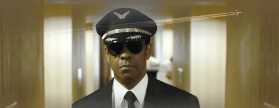 Film still from Flight: the pilot, played by Denzel Washington, walks down a hallway in sunglasses and cap, a jet contrail arcing above him.