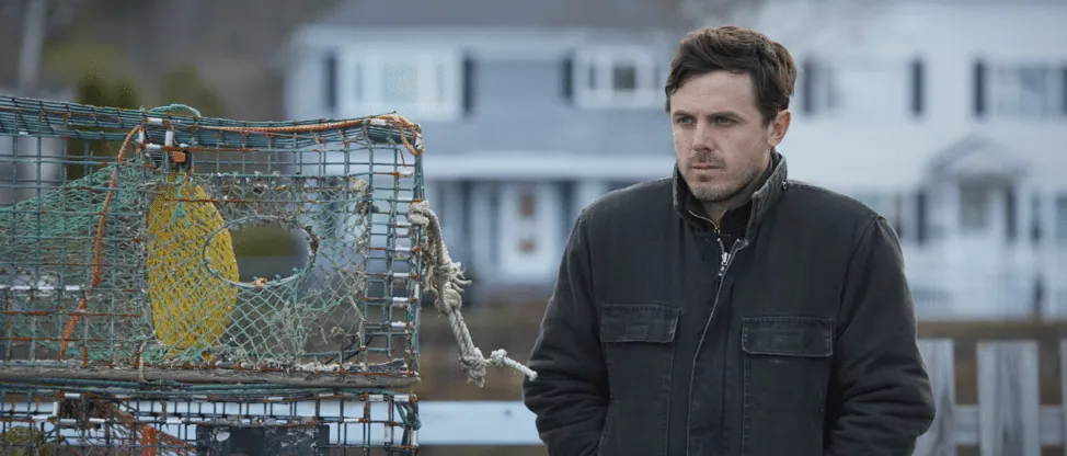 Film still from Manchester by the Sea: Lee stands beside a lobster trap on the dock, looking off into the distance.