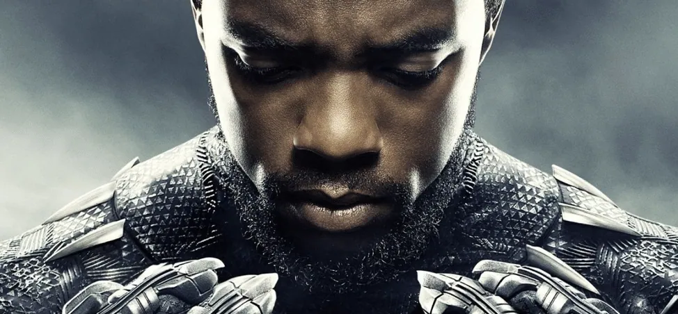 Film still from Black Panther: T'Challa, in his armored suit, bows his head in a close-up shot.