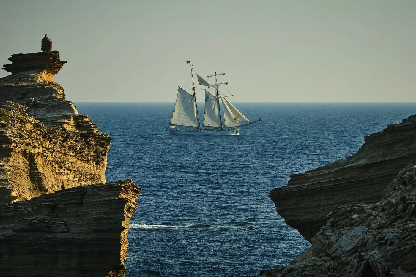 A tall sailing ship passing between rocky cliffs, evoking Treasure Island.