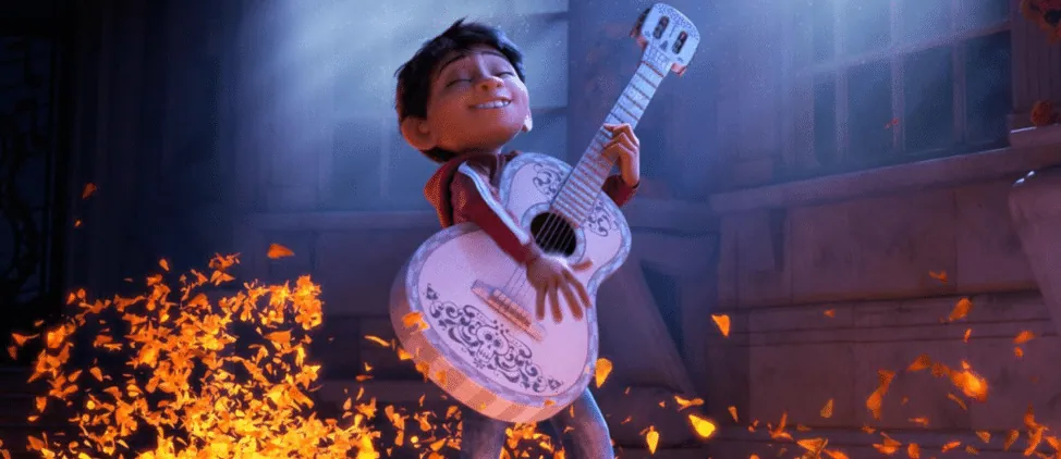 Animated still from Coco: Miguel joyfully strums his guitar as glowing marigold petals swirl around him.