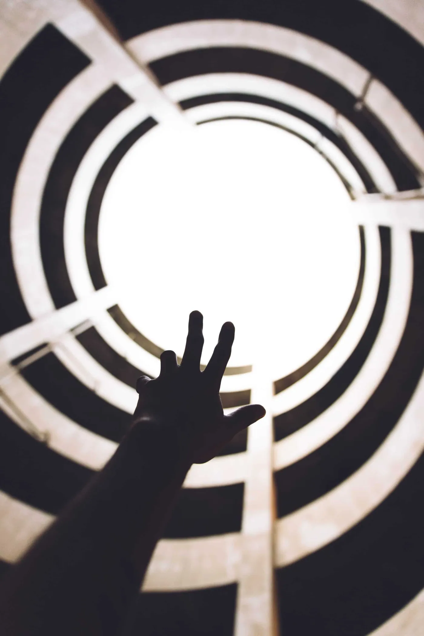 A hand reaching up toward bright light through a spiral stairwell shaft.