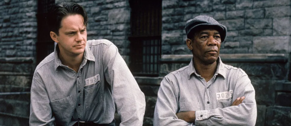 Film still from The Shawshank Redemption: Andy and Red stand together in the prison yard in their striped uniforms.