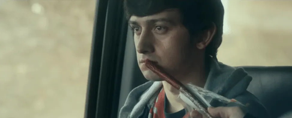 Film still from The Fundamentals of Caring: a young man sits in a car, blood on his lip, holding a metal rod.