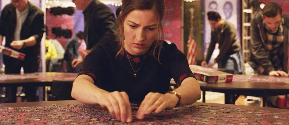Film still from Puzzle: a woman concentrates while assembling a jigsaw puzzle at a competition table.