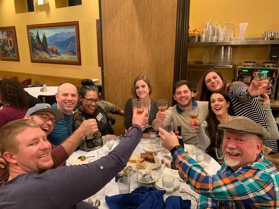 A group raising glasses in a toast around a restaurant table at The Sell More Books Show Summit 2019.