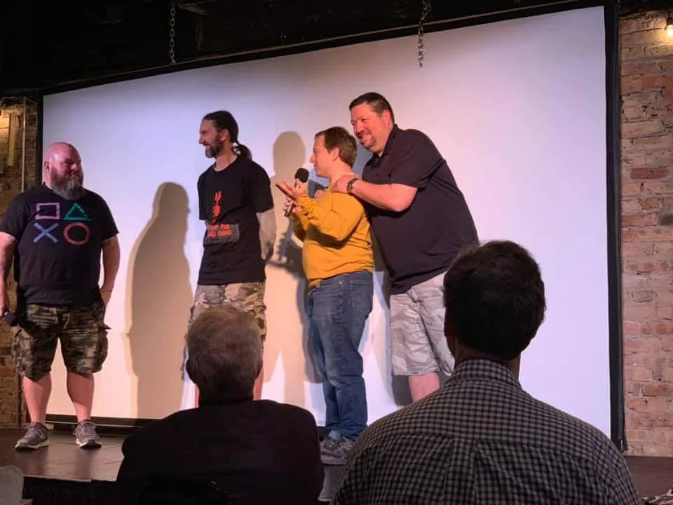 Four hosts of The Sell More Books Show Summit 2019 on stage, one holding a microphone.