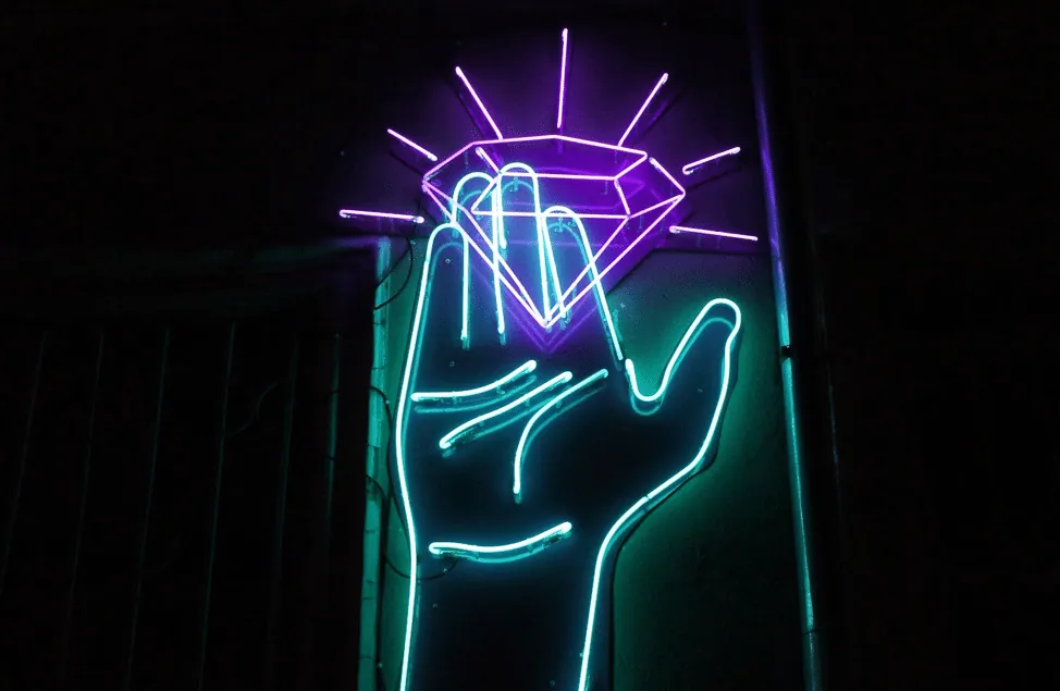 A neon sign of an open hand holding up a glowing purple diamond.