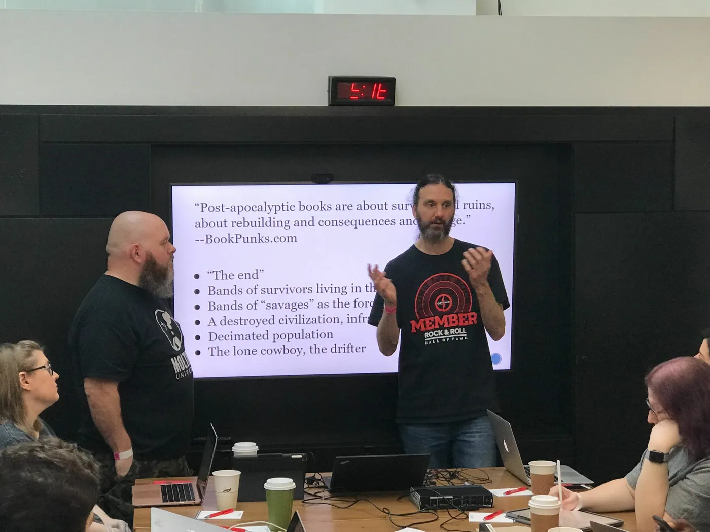 Two presenters discussing post-apocalyptic worldbuilding tropes on a slide at Rock Apocalypse 2019.