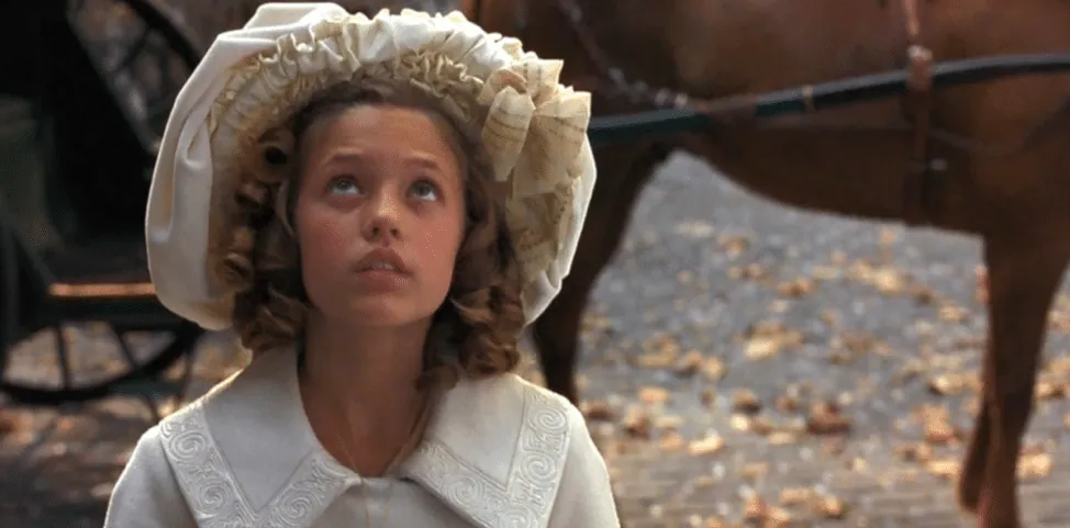 Film still from A Little Princess: young Sara Crewe, in a bonnet, gazes upward near a horse-drawn carriage.