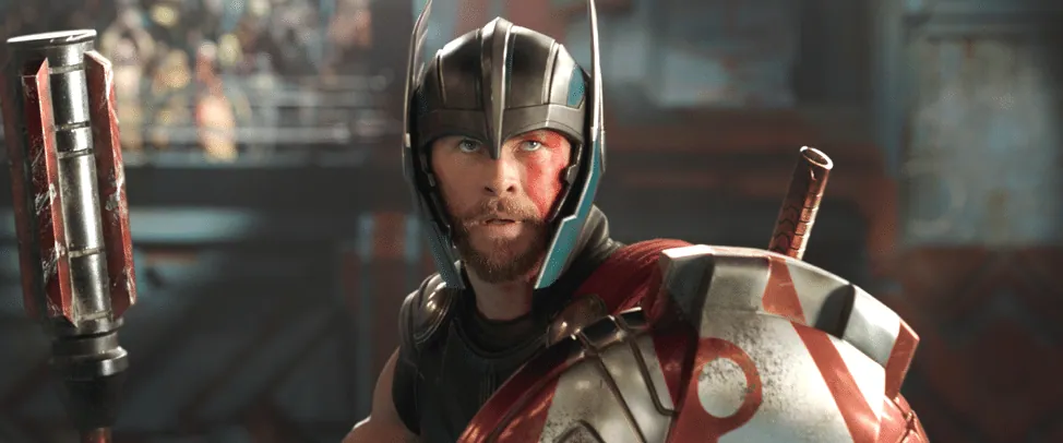Film still from Thor: Ragnarok: Thor, helmeted and armored, grips his weapon and shield in a gladiatorial arena.