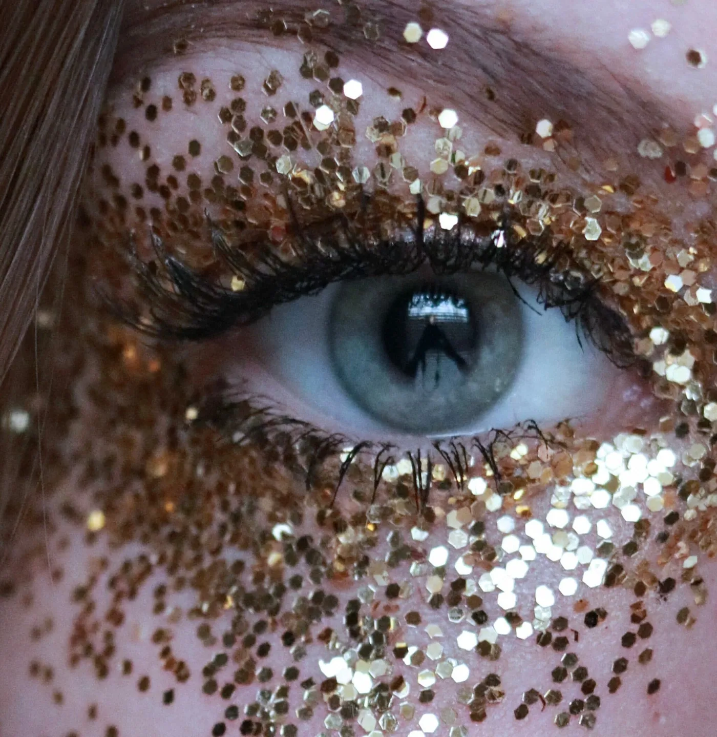 Extreme close-up of an eye with gold glitter scattered across the eyelid and cheek.