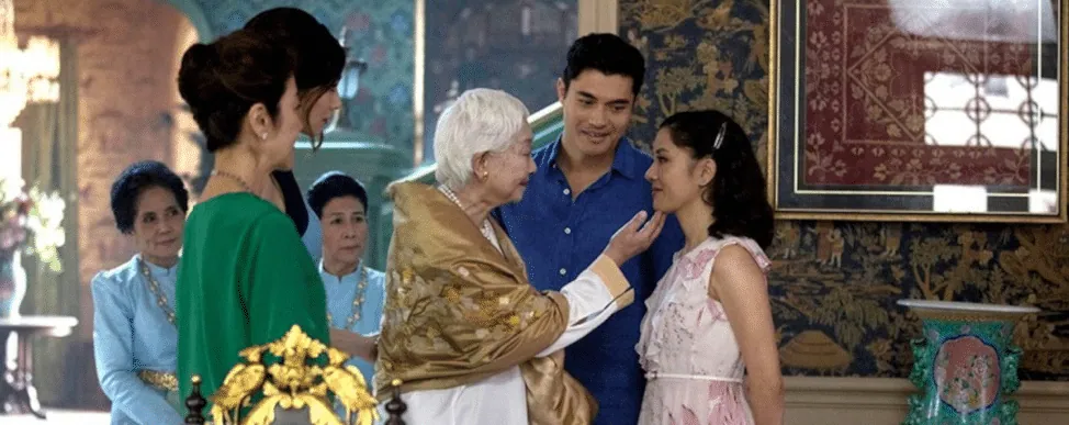 Film still from Crazy Rich Asians: the family matriarch tenderly touches Rachel's face as others look on.