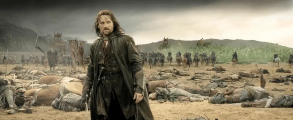 Film still from The Return of the King: Aragorn stands before a battlefield strewn with fallen soldiers as riders approach.