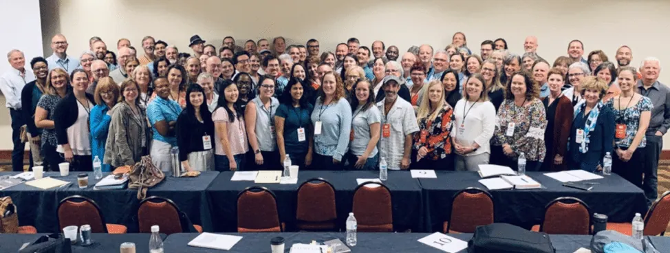 Group photo of attendees at the Story Grid Live 2019 conference, gathered around conference tables in a hotel ballroom.