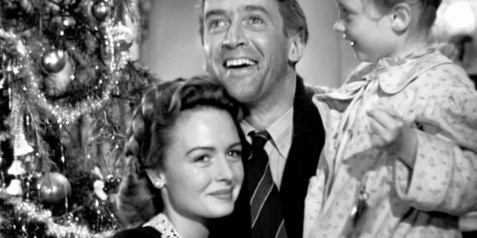 Film still from It's a Wonderful Life: George Bailey smiles with his wife and daughter beside the Christmas tree.