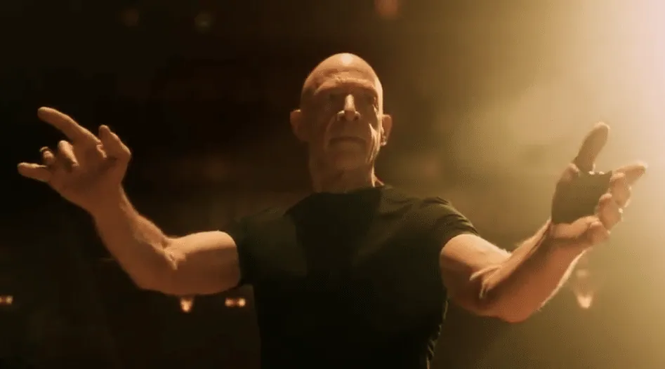 Fletcher (J.K. Simmons) conducting the band in Whiplash with both arms raised.