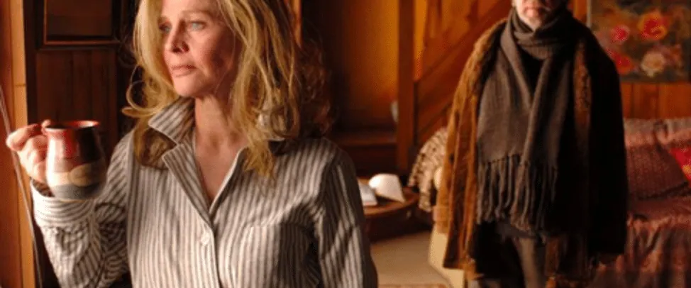 Film still from Away From Her (adapted from "The Bear Came Over the Mountain"): a woman holding a coffee mug with a man in a scarf behind her.