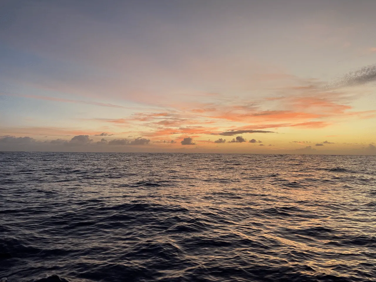 The ocean horizon at sunset, with soft orange light along a line of low clouds.