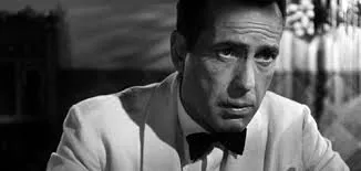 A black-and-white film still of a man in a white dinner jacket and bow tie, looking troubled — Rick from Casablanca.