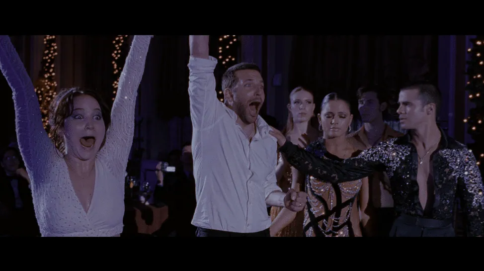 Film still from Silver Linings Playbook: Pat and Tiffany raise their arms in celebration at the dance competition, other dancers behind them.