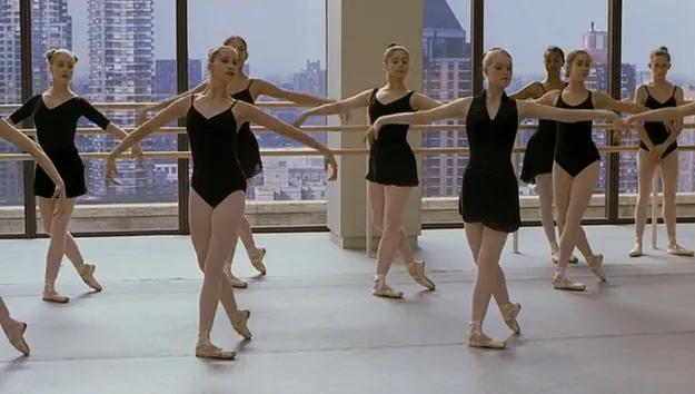 Film still from Center Stage: a line of ballet dancers practice at the barre in a studio overlooking the city skyline.