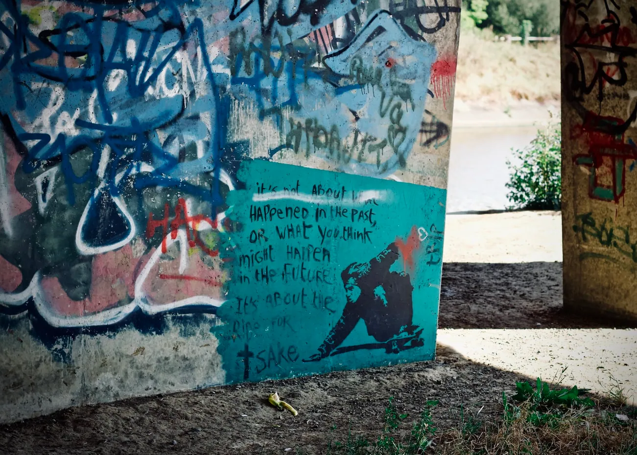 Modern graffiti stencil of a person crouched with a skateboard, spray-painted with a red heart above, beside the text "It's not about what happened in the past, or what you think might happen in the future. It's about the ride, for f*** sake."