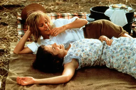 Film still from Fried Green Tomatoes: Idgie and Ruth lie together laughing on a picnic blanket in a field.