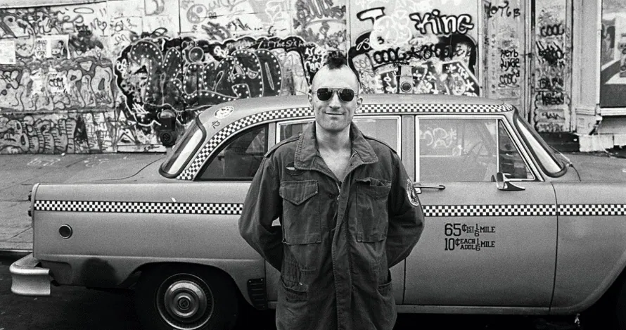 Robert De Niro as Travis Bickle, mohawk haircut, standing beside his taxi on a graffiti-covered street.
