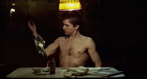 Travis Bickle testing his concealed spring-loaded gun holster mechanism at a table.