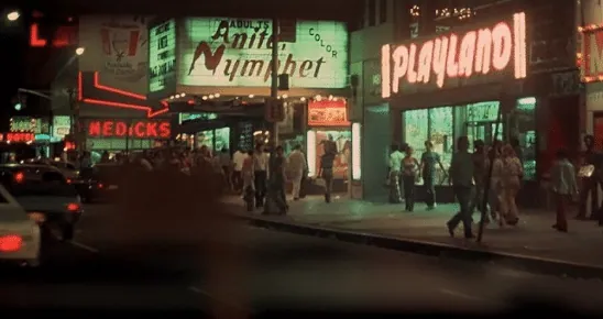 A 1970s New York City street at night, lined with neon signs and adult-theater marquees.