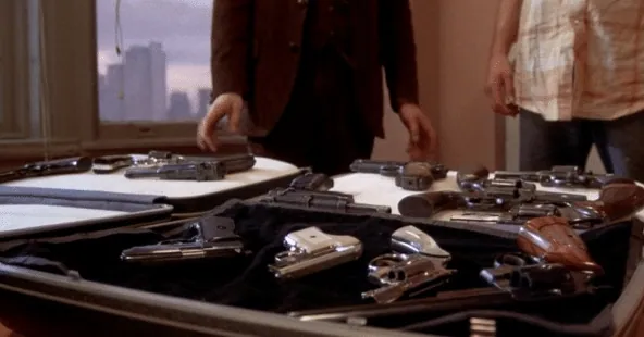 A briefcase spread open on a bed displaying rows of handguns for sale.