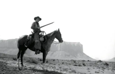 A cowboy on horseback carrying a rifle across a desert landscape, from the Western film The Searchers.