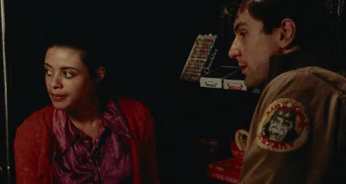 Travis Bickle speaking to a young woman at a concession counter inside a dim theater.