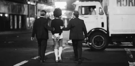 Two men flanking and gripping a young woman as they walk down a street at night, part of Taxi Driver's grim 1970s New York backdrop.