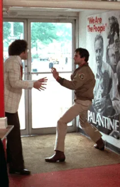 Travis dropping into a martial-arts stance to confront Tom in the campaign office doorway, with campaign posters behind them.