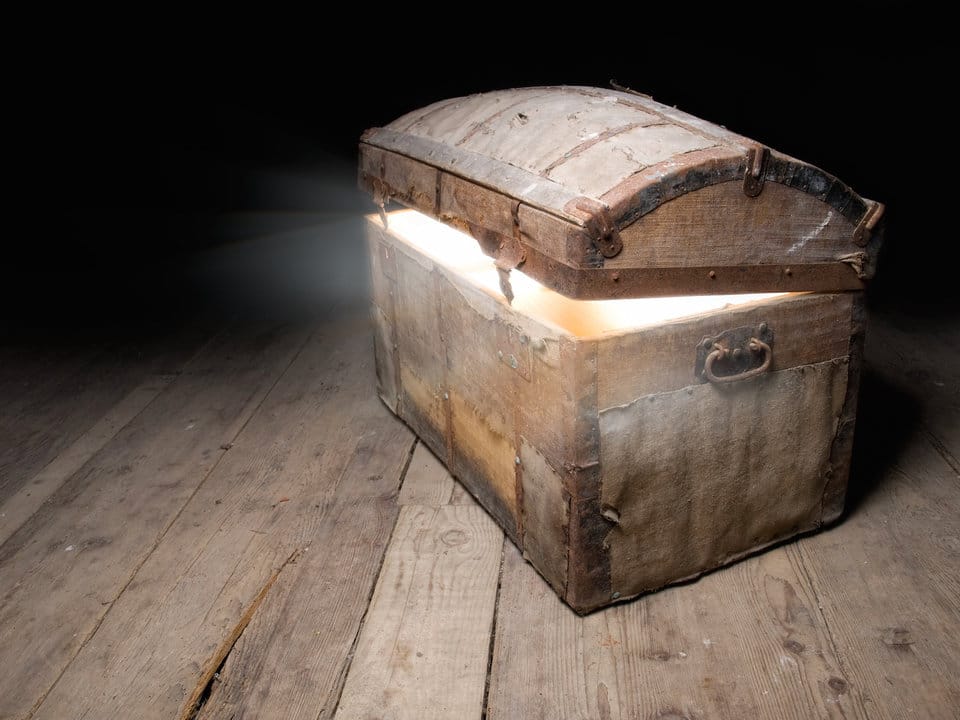 An antique wooden chest on a distressed wood plank floor, just cracked open with bright white light spilling out.